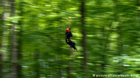 In a forest someone in a climbing harness is on a rope slide