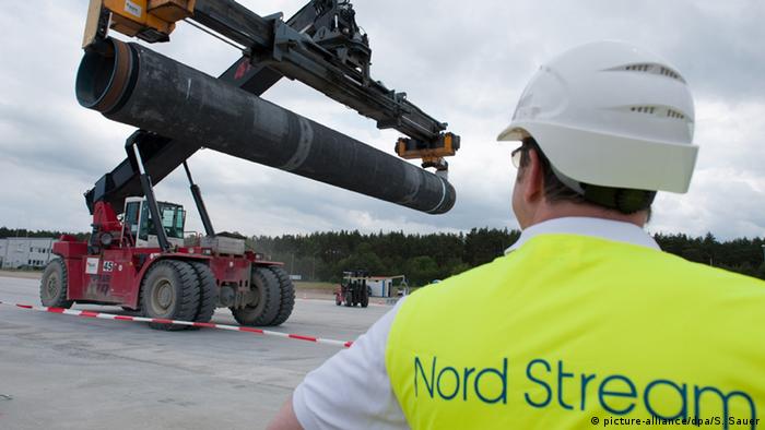 Рабочий в фирменной одежде Северного потока наблюдает за погрузкой трубы для газопровода