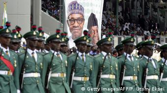 Soldiers march past a poster showing President Mohammadu Buhari