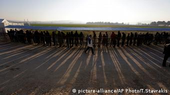 A long line of refugees cast long shadows as they wait for Food in Macedonia.