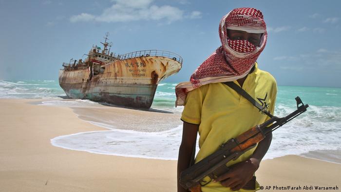 Африканский морской пират на фоне ржавеющего у берега судна