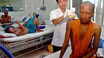 A nurse places a hot compress onto the shoulder of a Thai Buddhist monk
