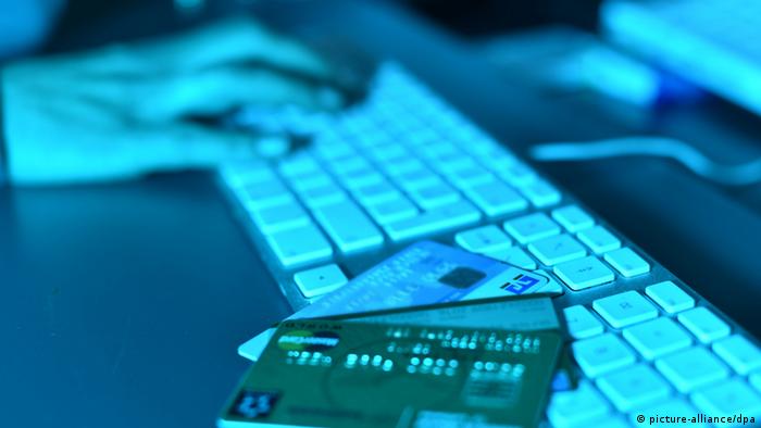 В полумраке кредитные карты лежат на компьютерной клавиатуре, на заднем плане человеческая рука