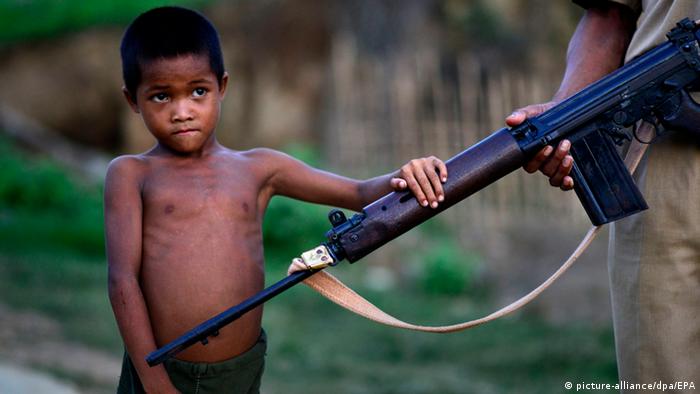 Ein kleiner Junge von vielleicht sechs Jahren hält seine kleine Hand auf das Maschinengewehr eines Soldaten, der nicht mehr ganz im Bild zu sehen ist. (Foto:picture-alliance/dpa/EPA)