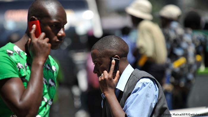 Two men on the street hold mobile phones to their ears
