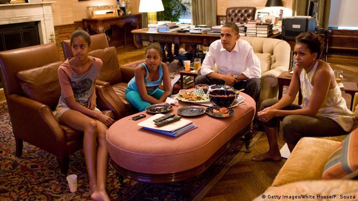 US-Präsident Barack Obama sitzt mit seiner Ehefrau Michele und seinen beiden Töchtern zusammen vor dem Fernseher mit einer Pizza. (Foto: picture alliance/dpa/Pete Souza)