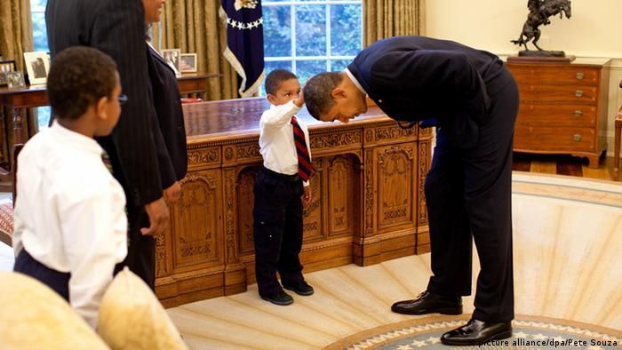 US-Präsident Barack Obama beugt sich zu einem kleinen Jungen herunter, der ihm über den Kopf streifen darf. Daneben steht ein weiterer Junge mit seinem Vater. (Foto: Official White House Photo/Pete Souza/CC BY 2.5 )