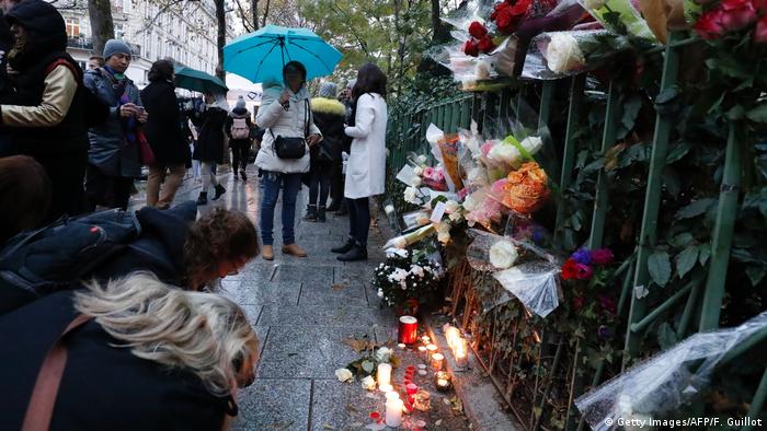 Personas se reúnen alrededor de flores y velas colocadas al lado de la sala de conciertos de Bataclan en París