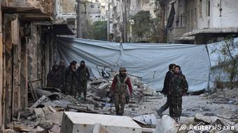 Syrian government soldiers walk amid rubble of damaged buildings after taking control of al-Sakhour neighborhood in Aleppo