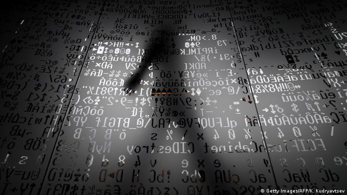 Тень человека на фоне стеклянной стены с символами программного кода