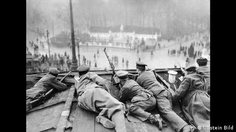 Το Βερολίνο σε εμφύλιο πόλεμο. Μια γενική απεργία είχε παραλύσει την πρωτεύουσα. Ένοπλοι περιπολούσαν στους δρόμους. Ο φωτογράφος Βάλτερ Γκίρκε έστρεψε το φακό του σε στρατιώτες που είχαν πάρει θέση πάνω στην Πύλη του Βρανδεμβούργου κατά τη διάρκεια της εξέγερσης των Σπαρτακιστών τον Ιανουάριο του 1919. 