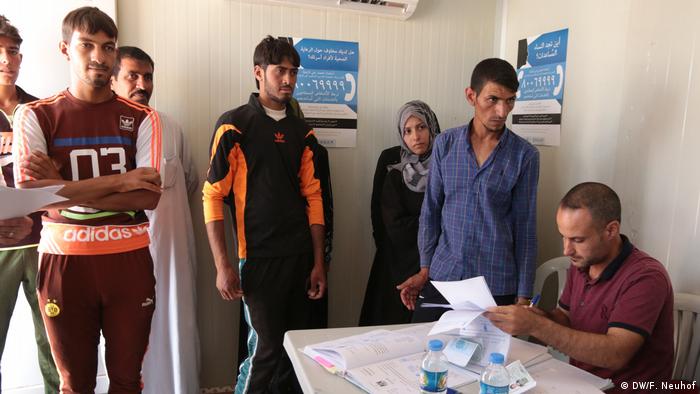 People wait for their certificates to be issued by a mobile court set up in a container in Hassansham camp