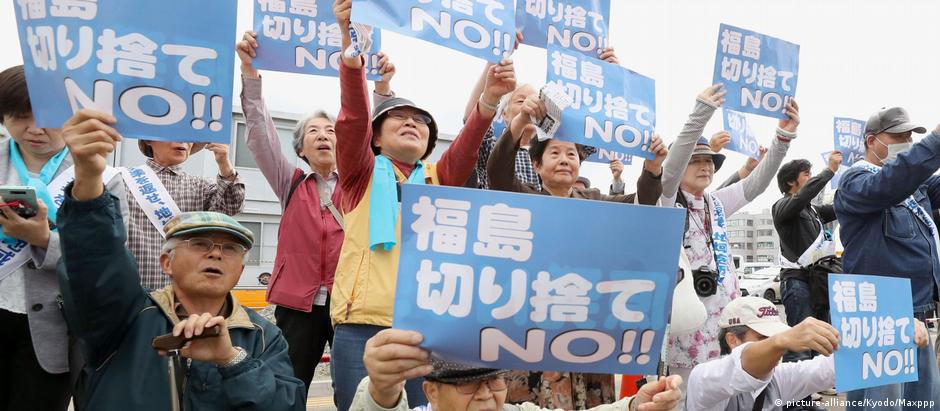 Alguns dos 3.800 requerentes da ação coletiva seguram cartazes do lado de fora do tribunal distrital de Fukushima