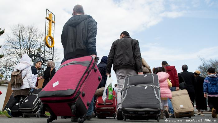 Syrian refugees pulling suitcases toward an asylum center in Germany