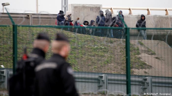 Migrants at Calais, police officers walking past (Reuters/P. Rossignol)