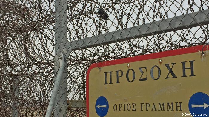 A refugee's torn glove hangs from the fence that divides Greece and Turkey next to a sign that reads: 'Beware: Greek-Turkish borderline'