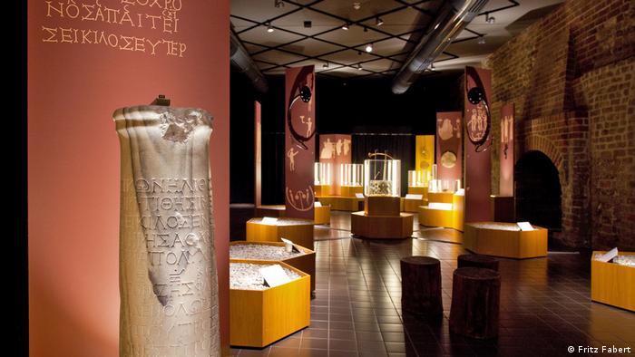A stone with ancient Greek writing is on the left in an exhibition with other objects (Fritz Fabert)