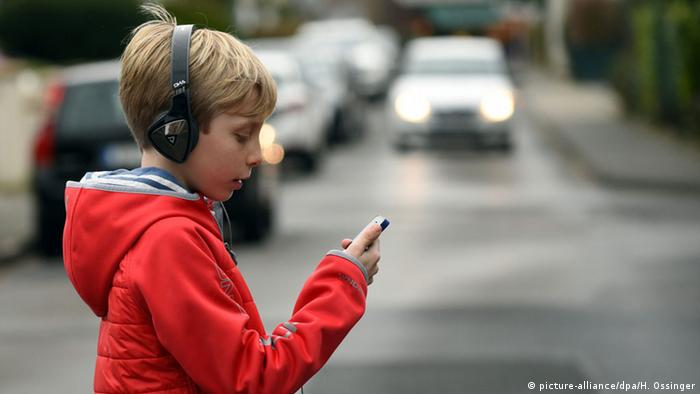 Menino com fone de ouvido e celular atravessando a rua