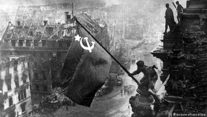 A Soviet soldier flies the Soviet flag off the ruins of the Reichtags building over a destroyed Berlin (picture-alliance/dpa)