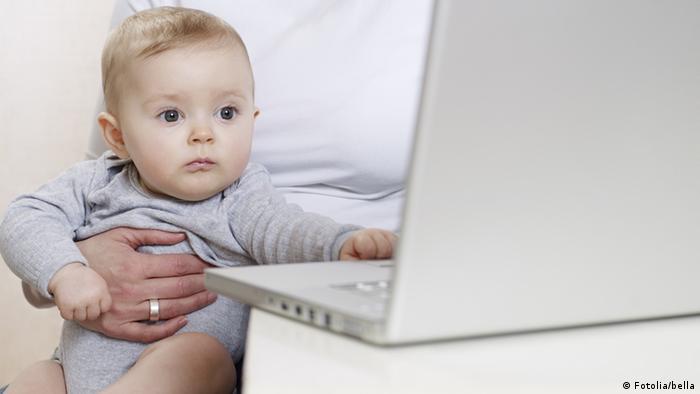 A woman holding a baby at a laptop computer (Fotolia/bella)