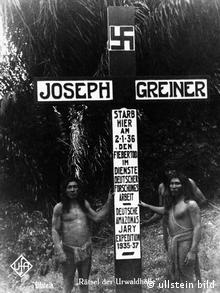 Indigenous people stand in front of a big cross with a swastika at the burial site of Joseph Greiner