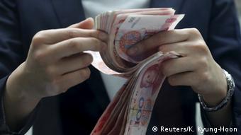 Человек пересчитывает пачку купюр в юанях