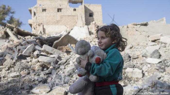 A girl holds a teddy bear amid the rubble in the Syrian town of Al Bab