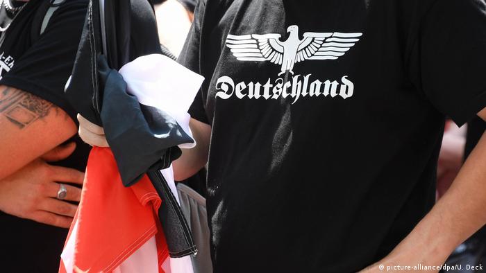Torsos masculinos com camisetas negras, estampadas em branco com uma águia e o dizer Deutschland
