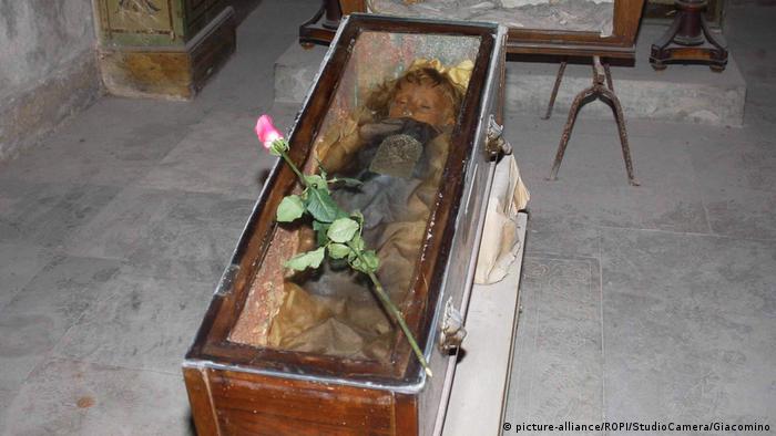 The mummy of Rosalia Lombardo in a glass coffin on which somebody placed a rose.