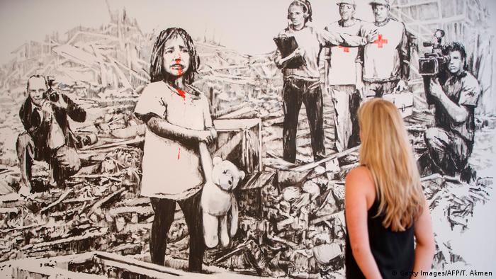 Black-and-white picture by Banksy showing child in ruins of war and media looking on (Getty Images/AFP/T. Akmen)