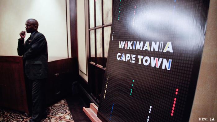 A man standing at near a doorway where a poster for Wikimania Cape Town is on display. (DW/J. Jaki)