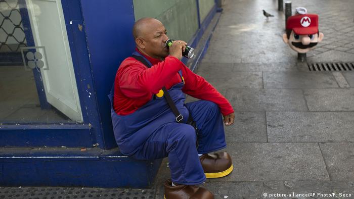 A man wearing a Mario Bros costume takes a break from work posing for tourist photos in the shade at Sol square in Madrid, Spain