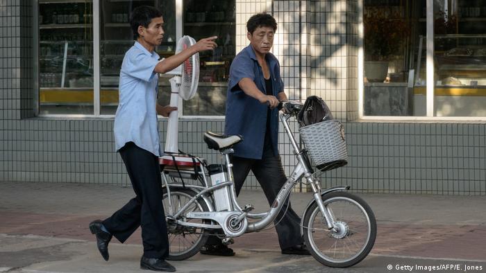 Two men push an electric bicycle carrying an electric fan along a street in Pyongyang, North Korea