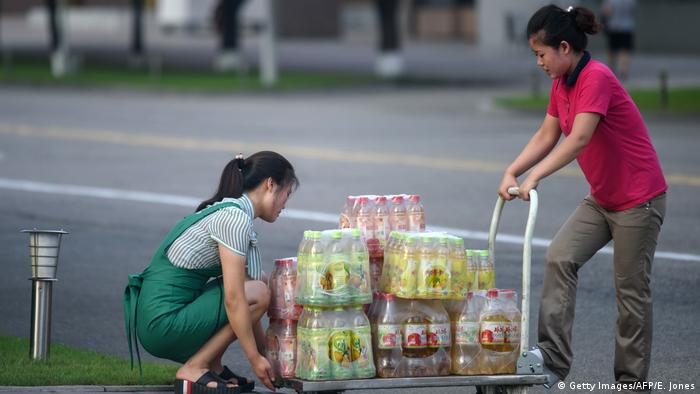 Women push a cart laden with North Korean soda drinks across a road in Pyongyang
