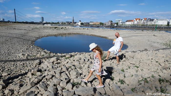 A family walks next to a puddle in the partially dried riverbed of Rhine, in front of the skyline of Dusseldorf, Germany