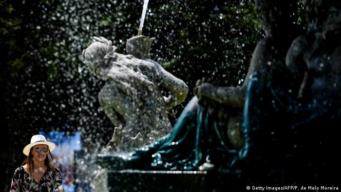 A woman sporting a hat walks past a fountain at Rossio square in Lisbon, Portugal