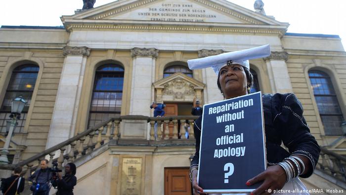 A woman wearing a traditional Herero head covering holds a placard that reads: Reparations without an official Apology? (picture-alliance/AA/A. Hosbas)