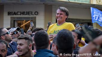 Bolsonaro, vestido de camisa amarela, faz expressão de dor em momento que levou facada