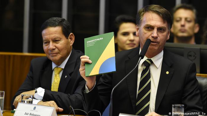 O presidente Jair Bolsonaro (à dir.) segura um exemplar da Constituição ao lado de seu vice, Hamilton Mourão