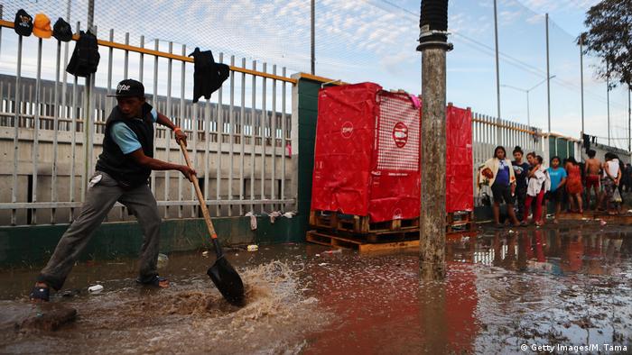 Funcionário tenta conter vazamento em abrigo em Tijuana, enquanto migrantes aguardam em fila para tomar banho