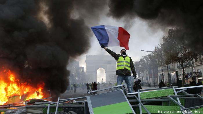 Manifestante dos coletes amarelos ergue a bandeira da FranÃ§a em barricada na avenida Champs-Ã‰lysÃ©es, em Paris