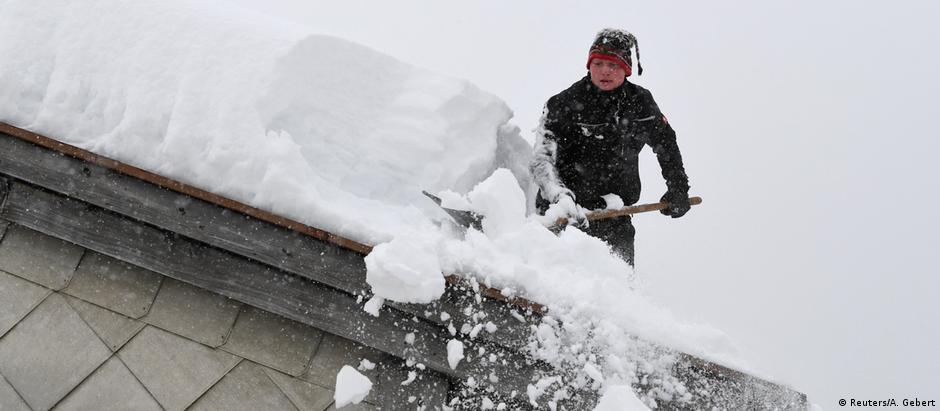 Homem remove camada de neve do telhado de sua casa em Inzell, na Alta Baviera