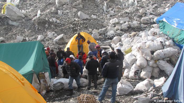 Hombres en el campamento base del Everest, rodeados de tiendas de campaña y bolsas de basura. 