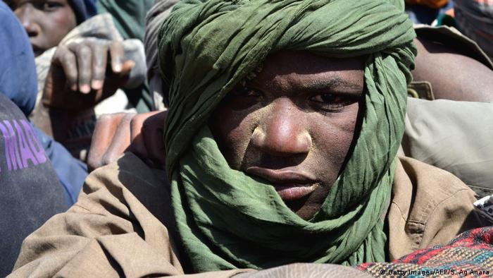 A young African man, his head wrapped in a scarf, looks out from a truck full of migrants (Getty Images/AFP/S. Ag Anara)
