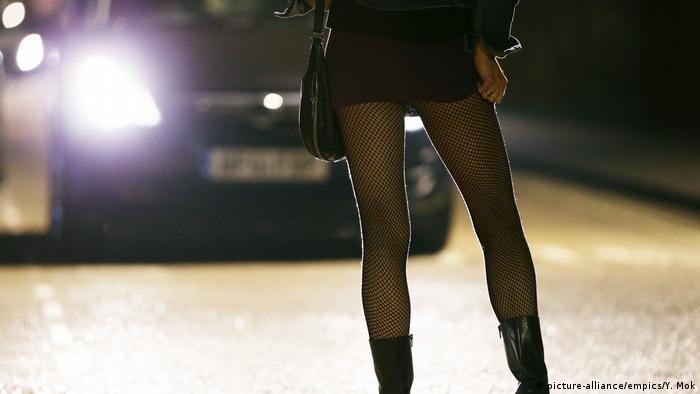 Проститутка стоит на дороге перед машиной со включенными фарами
