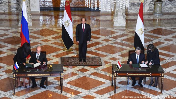 Ministers sign an agreement at tables with the Russian and Egyptian flags behind them