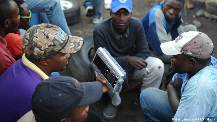 A group of men in DRC gather around a hand-held radio to listen to a broadcast