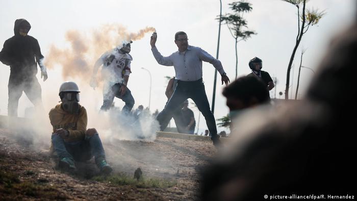 Homem com tarje civil arremessa bomba de gás lacrimogêneo nos arredores da base militar de La Carlota, em Caracas