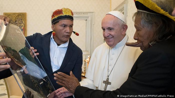 Na foto, líder indígena que vive no Xingu (à esquerda) mostra objeto ao Papa (centro). O cacique Raoni está à direita do pontífice