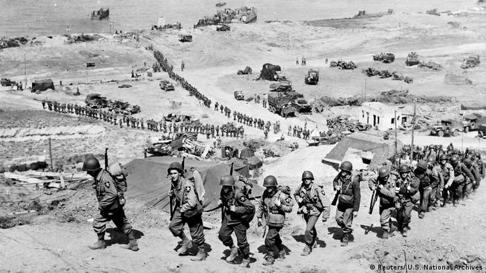 Soldados americanos marcham diante da praia de Omaha, em 18 de junho de 1944
